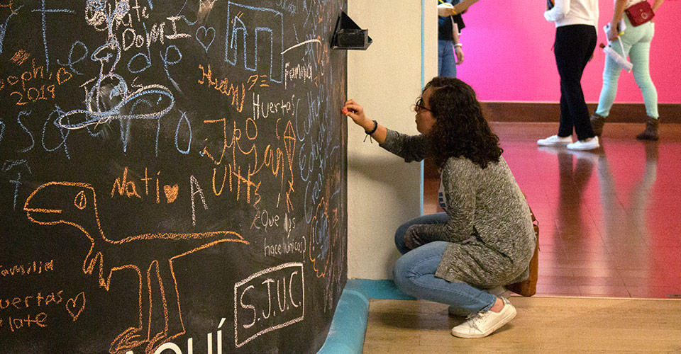 Visitante femenina interviniendo la pared del Salón educativo del Museo de Arte Costarricense con tizas de colores.